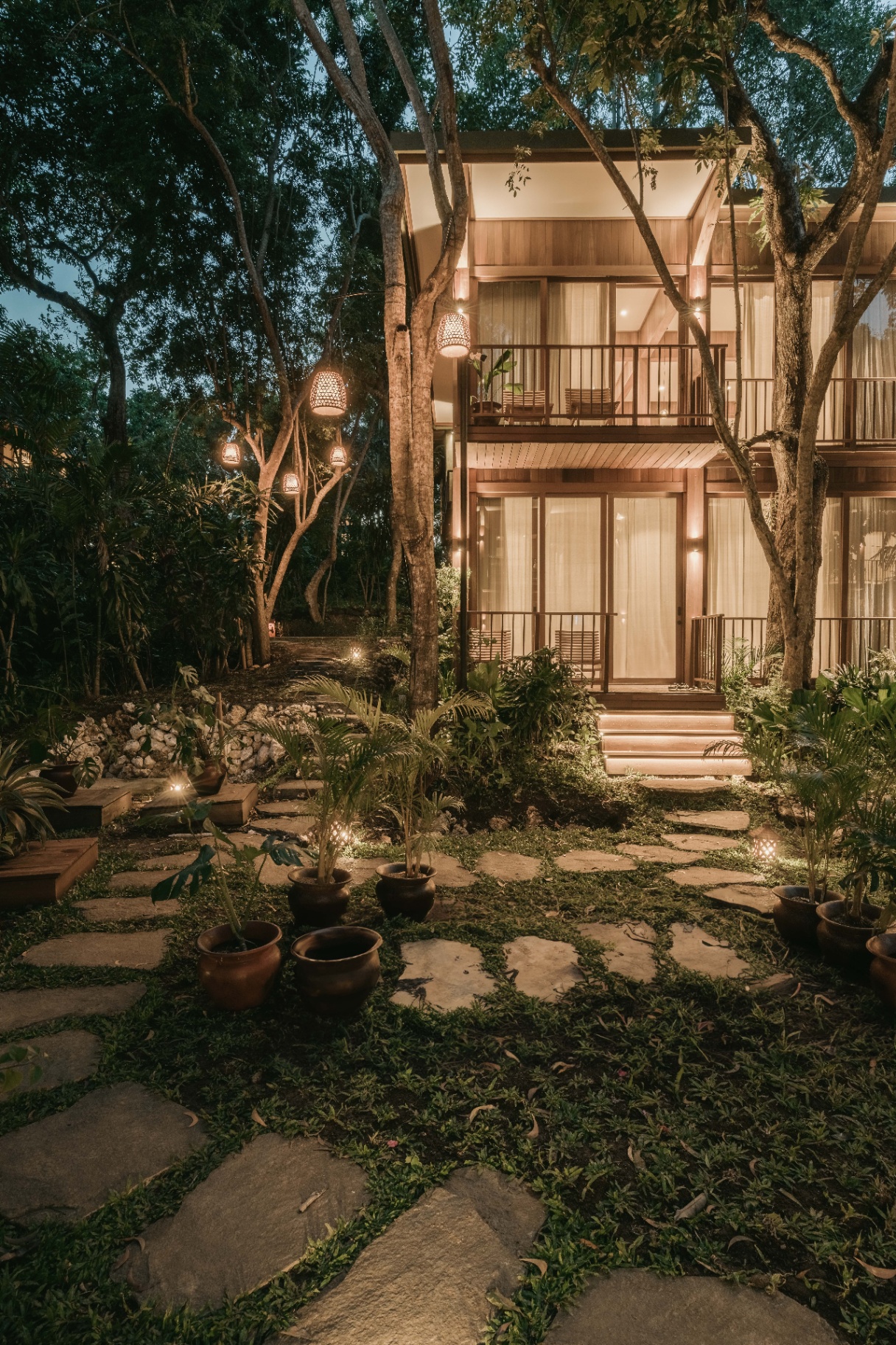Two-story villa lit warmly at dusk amid tropical gardens
